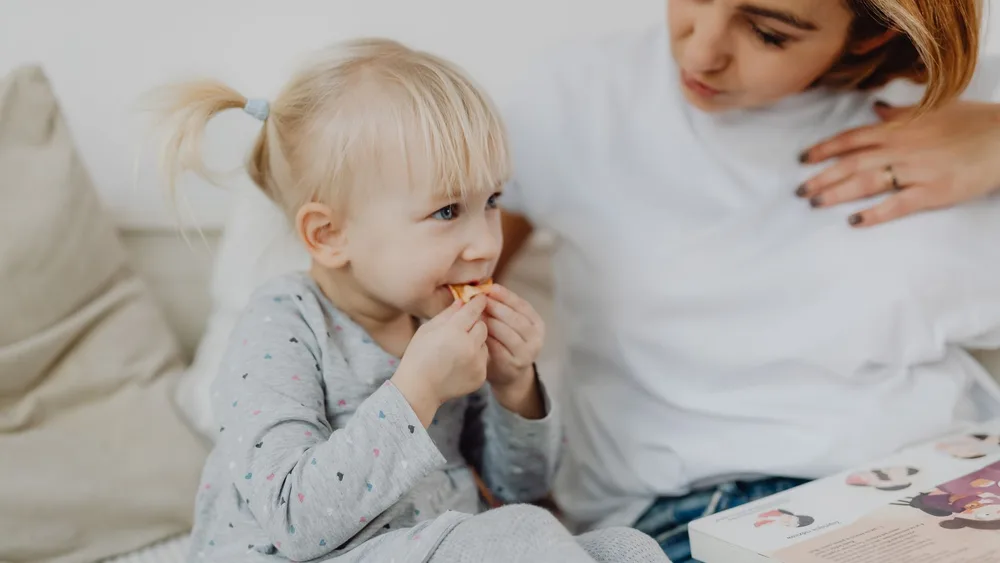 A woman and a toddler sharing a snack on a sofa
