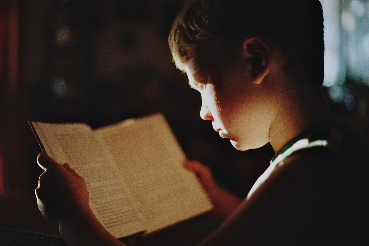 Boy reading a book by torchlight