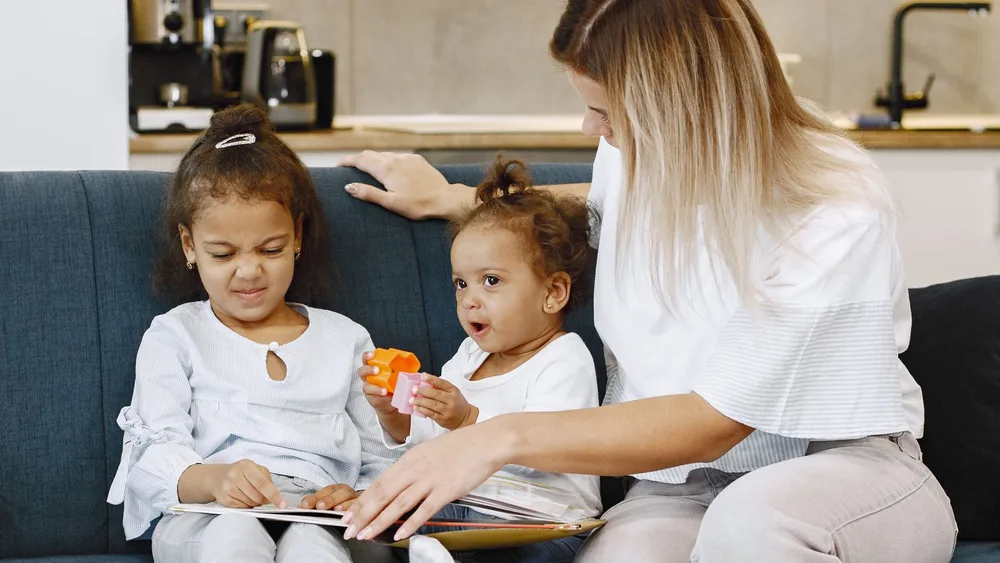 A woman sitting on a sofa looking at a picture book with two young children