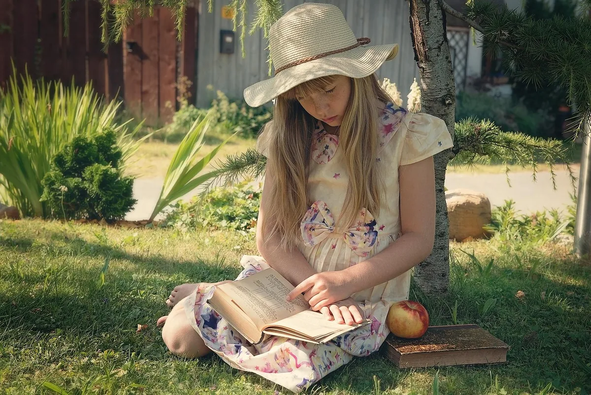 Girl in a sun hat reading a book in the garden